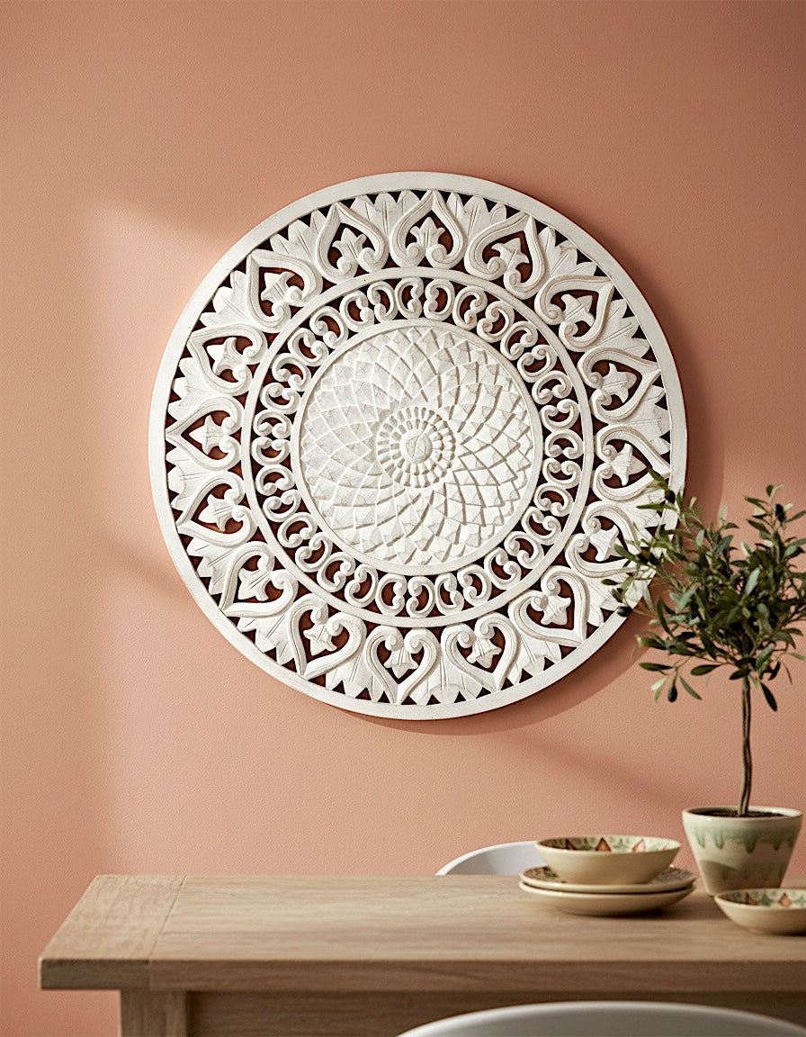 Decorative white wall art on a peach-colored wall with a wooden table and plant in the foreground.