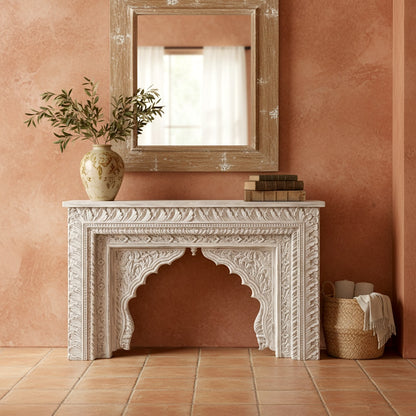 Decorative fireplace with a vase, books, and plant against a pink wall.